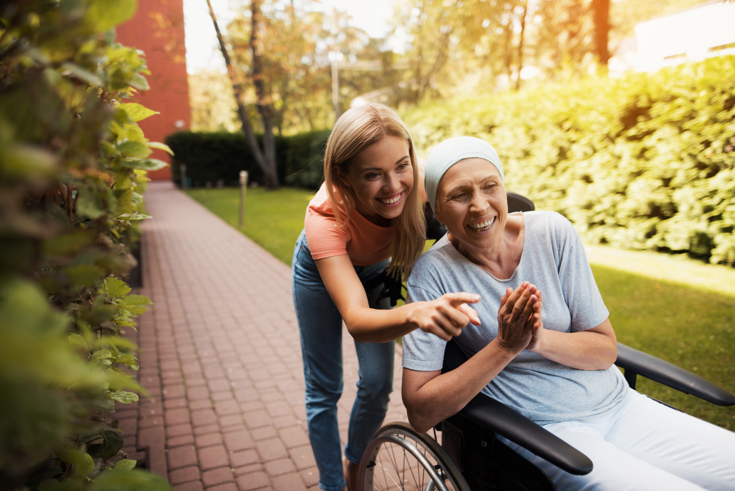 A woman with cancer sits in a wheelchair, being pushed by a nurse